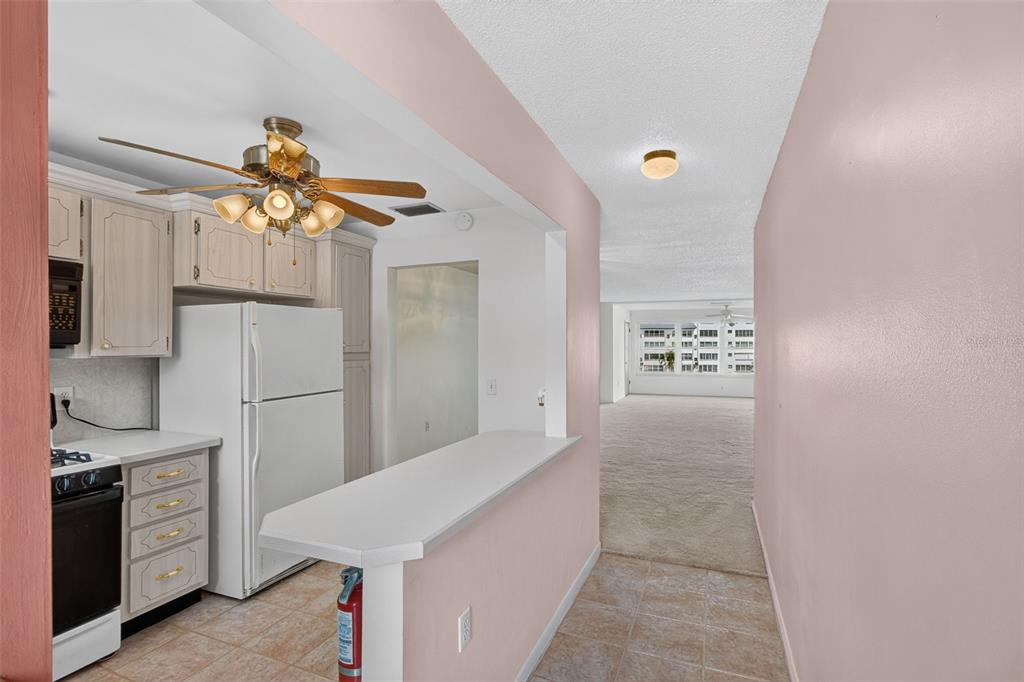 A kitchen features white cabinets, a breakfast bar with wooden chairs, and a ceiling fan — 6025 SHORE BOULEVARD S UNIT 303, GULFPORT, FL
