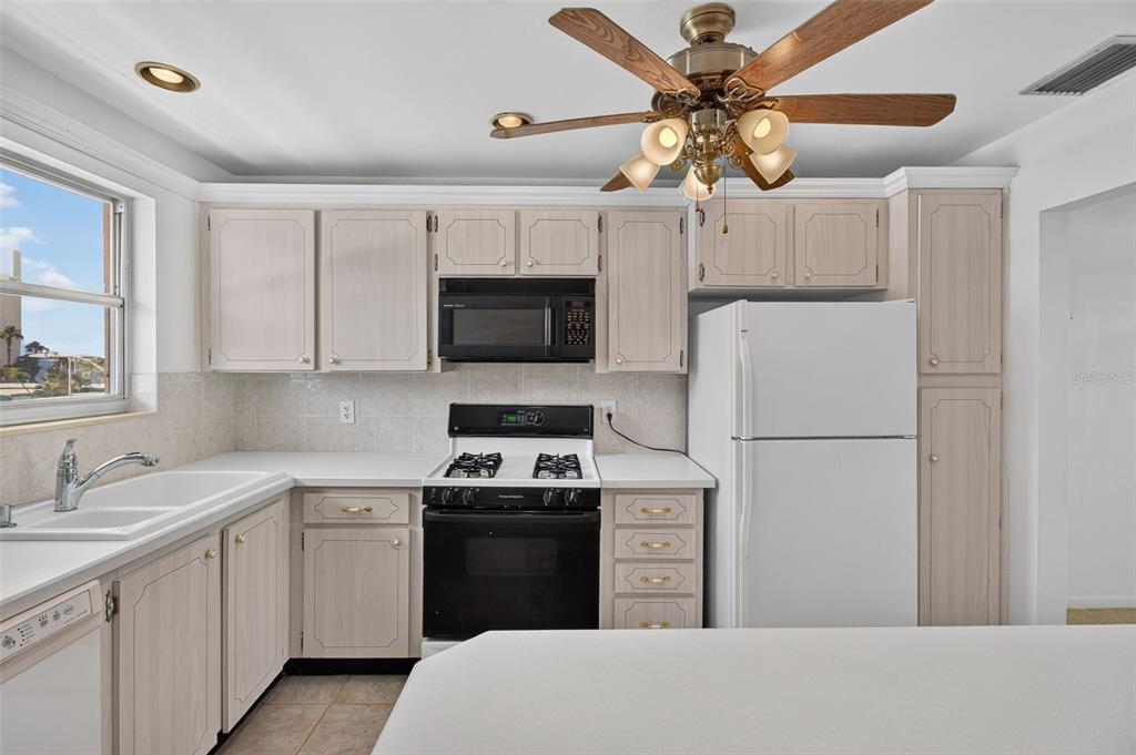 A kitchen features white cabinets, white appliances, a ceiling fan, and a breakfast bar — 6025 SHORE BOULEVARD S UNIT 303, GULFPORT, FL