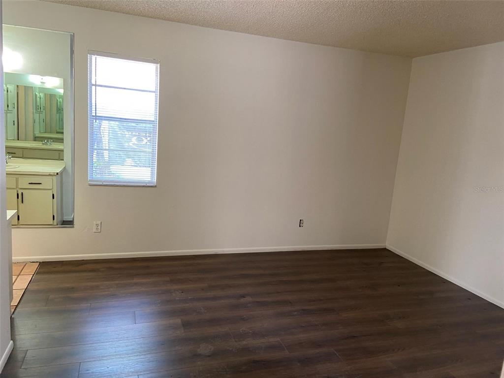 A room with dark wood-look flooring, white walls, a window, and a mirrored bathroom entrance — 3149 HURON AVENUE, OLDSMAR, FL