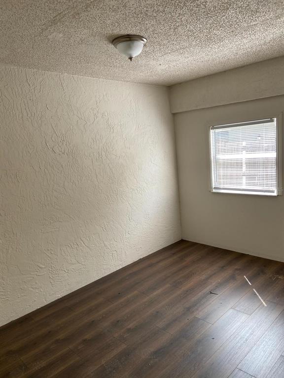 An empty room features dark wood-look flooring, textured walls, and a ceiling-mounted light fixture — 3149 HURON AVENUE, OLDSMAR, FL