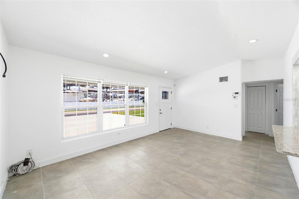 A bright, empty room features white walls, gray tile flooring, recessed lighting, and large windows — 3325 W SHELL POINT ROAD, RUSKIN, FL