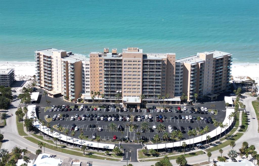 An aerial view shows a large beachfront condominium complex with a parking lot and palm trees — 880 MANDALAY AVENUE UNIT N610, CLEARWATER BEACH, FL