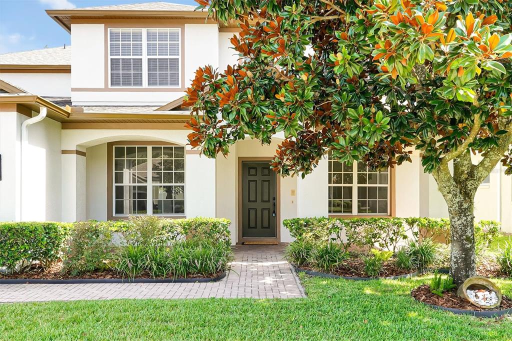 A two-story house exterior features a paved walkway, a dark front door, and a large tree — 554 PALIO COURT, OCOEE, FL