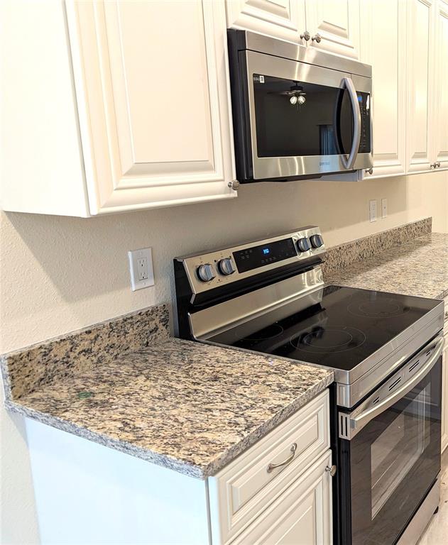 A kitchen features white cabinets, a stainless steel microwave, a glass-top stove, and granite countertops — 104 ROBERTS AVENUE, MULBERRY, FL