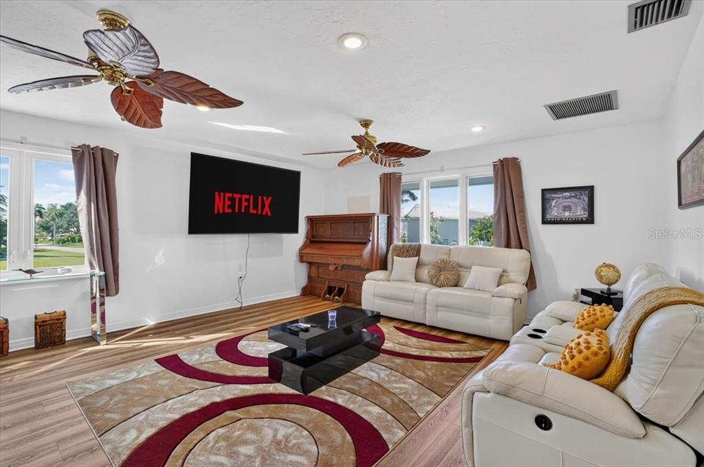 A living room features white walls, wood-look flooring, two ceiling fans, and a wall-mounted television — 2407 PALMA SOLA BOULEVARD, BRADENTON, FL