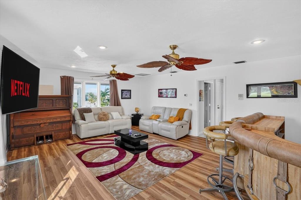 A living room features light-colored sofas, a patterned area rug, a wooden bar, and a television — 2407 PALMA SOLA BOULEVARD, BRADENTON, FL