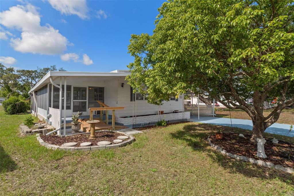 A white mobile home features a screened porch, a wooden ramp, and a large shade tree — 9075 HIGHPOINT BOULEVARD, BROOKSVILLE, FL