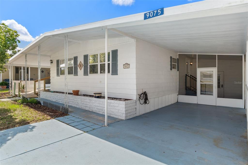 A white mobile home features a carport, a screened-in porch, and a brick planter box — 9075 HIGHPOINT BOULEVARD, BROOKSVILLE, FL