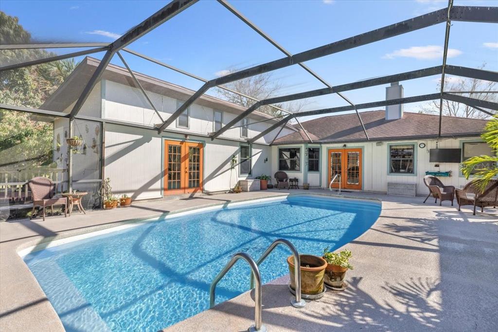 A swimming pool sits inside a screened-in patio area next to a house with doors — 281 OLD DIXIE HIGHWAY, VERO BEACH, FL