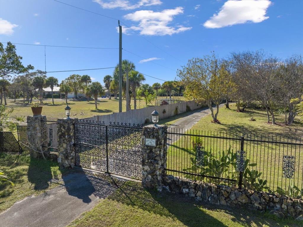 An iron gate with stone pillars opens to a long driveway on a grassy lot — 281 OLD DIXIE HIGHWAY, VERO BEACH, FL