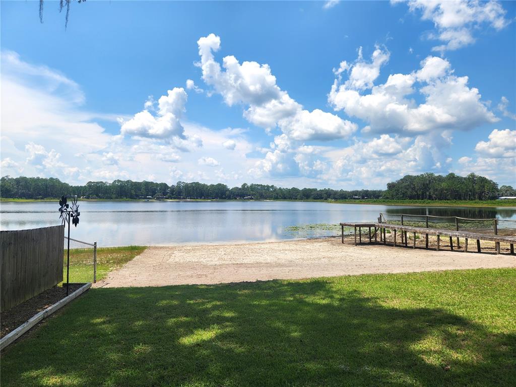 A sandy beach area leads to a wooden dock on a lake under a cloudy sky — 21994 NE 106TH AVENUE, FORT MC COY, FL