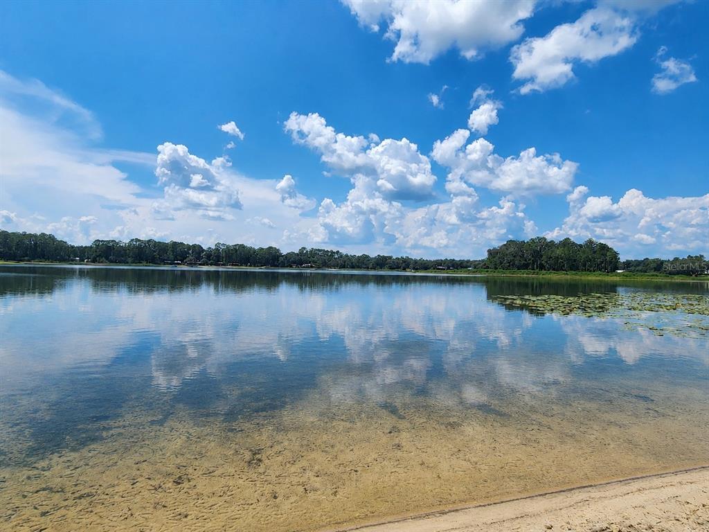 A sandy shoreline overlooks a calm lake reflecting the blue sky and white clouds — 21994 NE 106TH AVENUE, FORT MC COY, FL