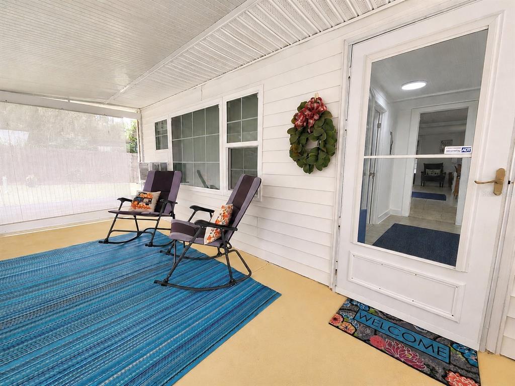 A covered porch features two rocking chairs, a blue area rug, and a white door — 21994 NE 106TH AVENUE, FORT MC COY, FL