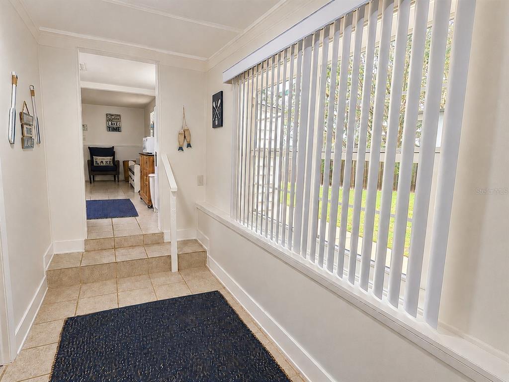 A tiled entryway with a step up to a hallway featuring vertical blinds and decor — 21994 NE 106TH AVENUE, FORT MC COY, FL