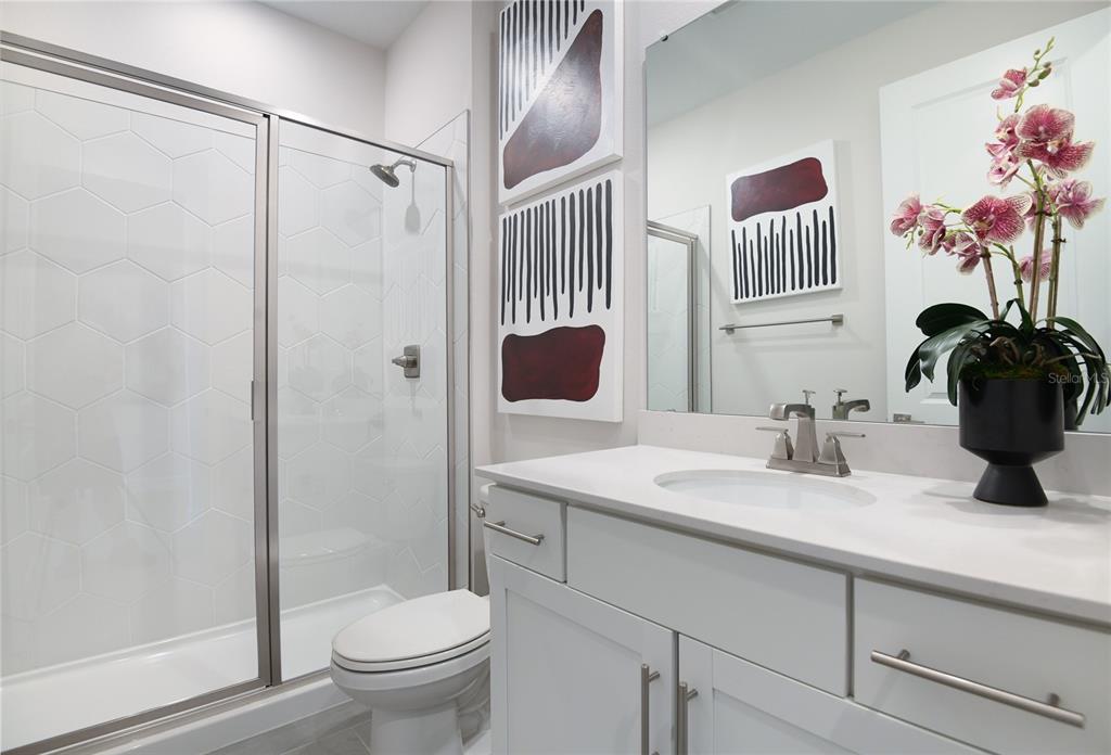 A bathroom features a glass-enclosed shower, a white vanity with a sink, and wall art — 3457 MACCHI AVENUE, TAVARES, FL