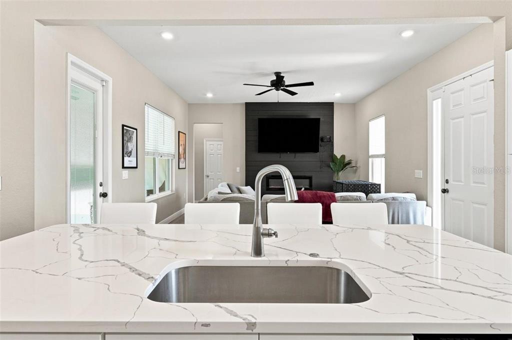 A kitchen island with a white marble countertop and sink overlooks a living room area — 795 CROSSTOWER DRIVE, WINTER HAVEN, FL