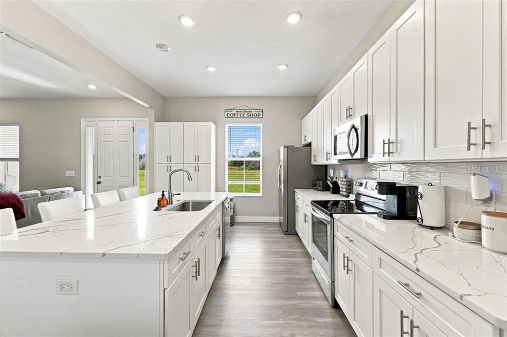A modern kitchen features white cabinetry, quartz countertops, a large island, and stainless steel appliances — 795 CROSSTOWER DRIVE, WINTER HAVEN, FL