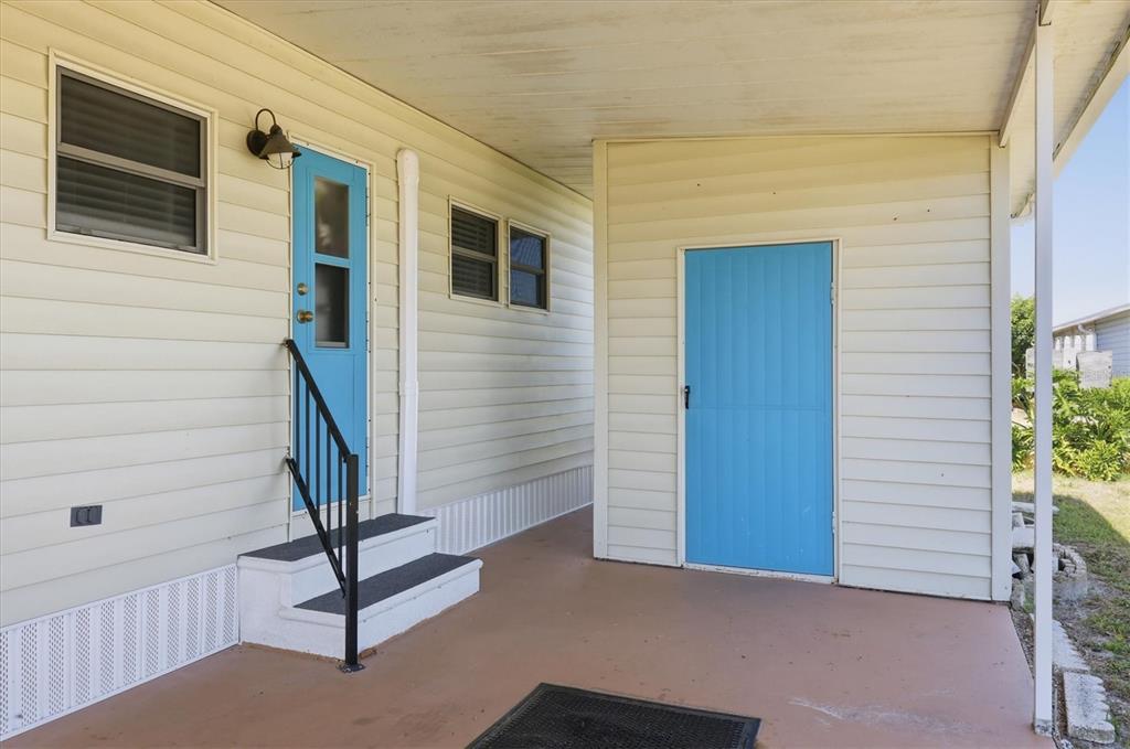 A covered patio features two bright blue doors, white siding, and a small set of stairs — 1107 44TH AVENUE DRIVE E, ELLENTON, FL