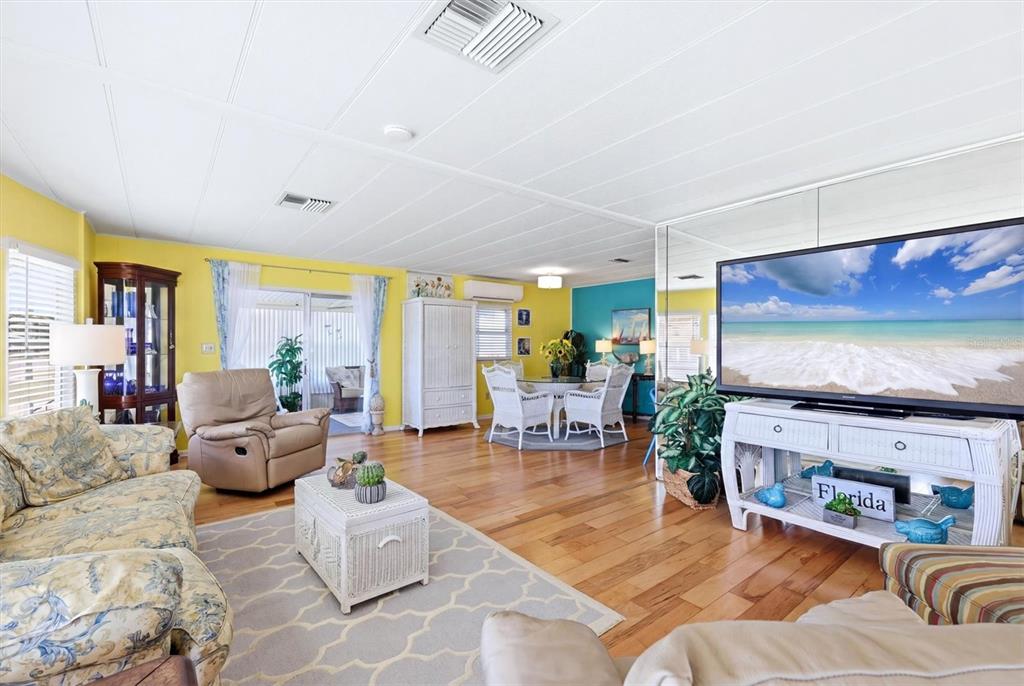 A living room features yellow walls, hardwood floors, a large television, and a dining area — 1107 44TH AVENUE DRIVE E, ELLENTON, FL