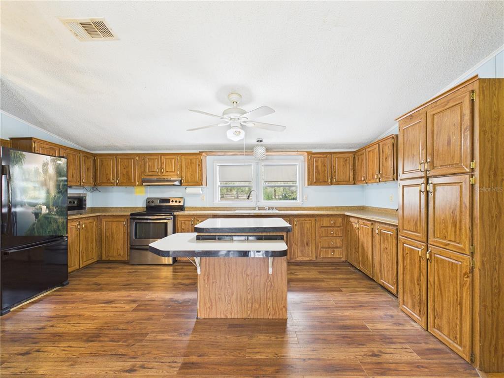A kitchen features wood cabinets, a central island, stainless steel appliances, and wood-look flooring — 7085 S RHODER POINT, LECANTO, FL