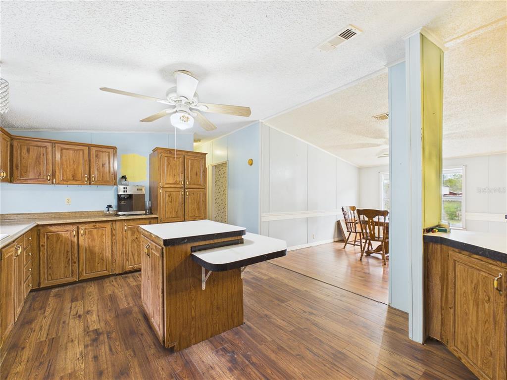 A kitchen with wood cabinets, a center island, and wood-look flooring opens to a dining area — 7085 S RHODER POINT, LECANTO, FL