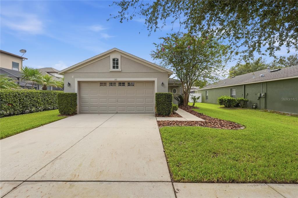 A single-story house with a beige stucco exterior, a two-car garage, and a concrete driveway — 311 WESTCHESTER HILLS LANE, VALRICO, FL