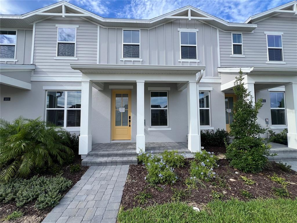 A two-story townhouse exterior features light gray siding, a yellow front door, and a stone walkway — 1819 PINECLIFF DRIVE, APOPKA, FL