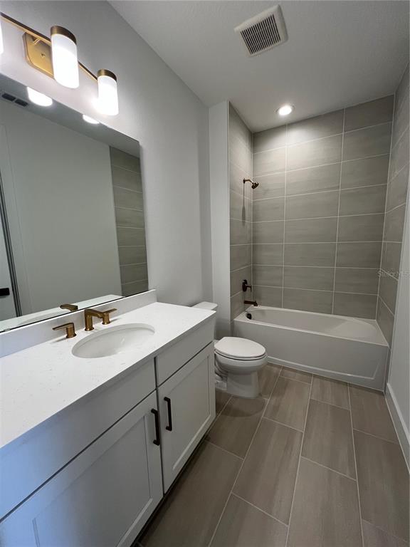 A bathroom features a white vanity with gold fixtures, a tiled tub-shower combo, and gray flooring — 1819 PINECLIFF DRIVE, APOPKA, FL