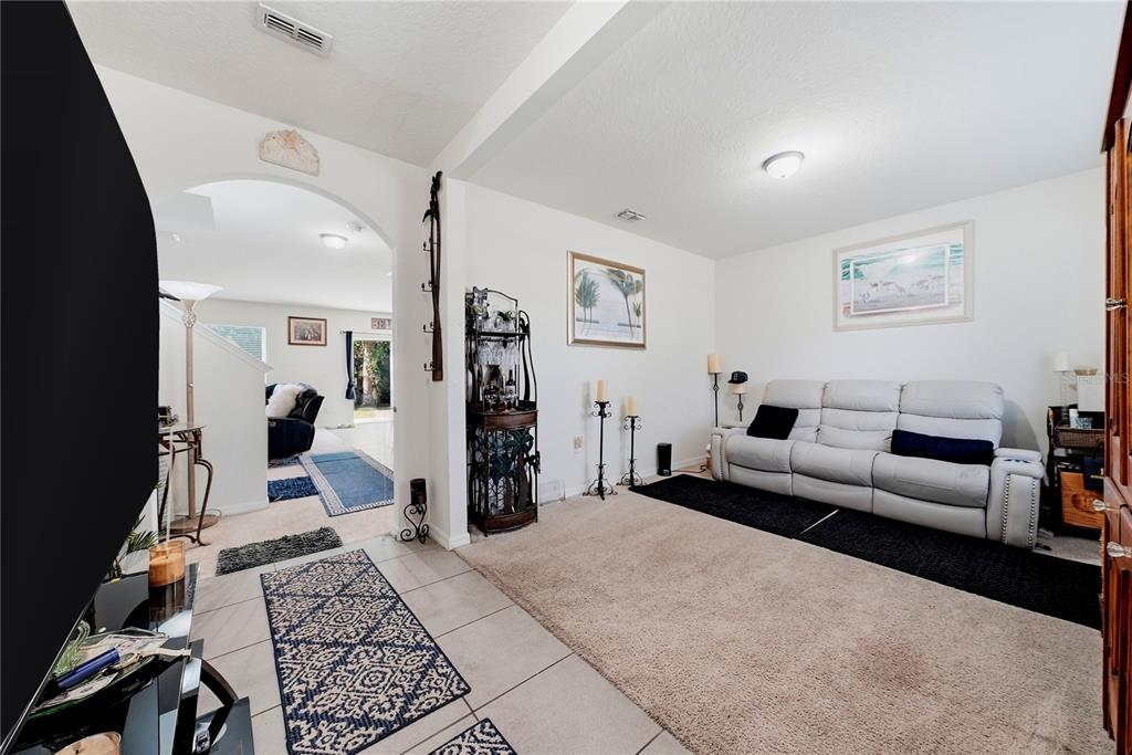 A living room features a white sofa, beige carpet, tile flooring, and an arched entryway — 8128 HARWICH PORT LANE, GIBSONTON, FL