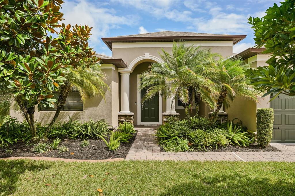 The exterior of a tan house features a stone-accented entryway, columns, and lush landscaping — 2841 AUTUMN BREEZE WAY, KISSIMMEE, FL