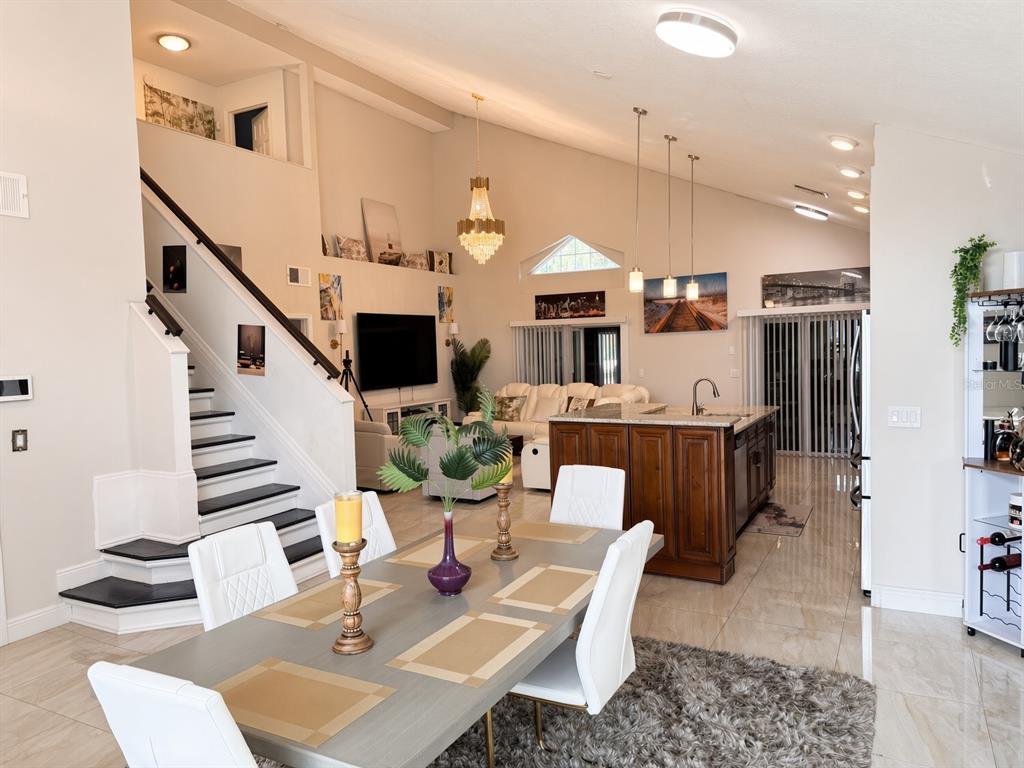 An open-concept living area features a dining table, kitchen island, and staircase with dark treads — 3010 STILLWATER DRIVE, KISSIMMEE, FL