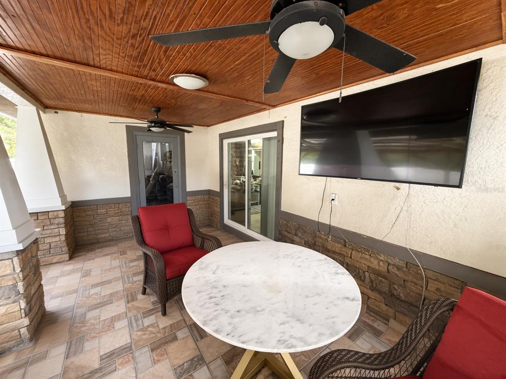 A covered patio features a stone-accented wall, a mounted television, and a round marble table — 3010 STILLWATER DRIVE, KISSIMMEE, FL