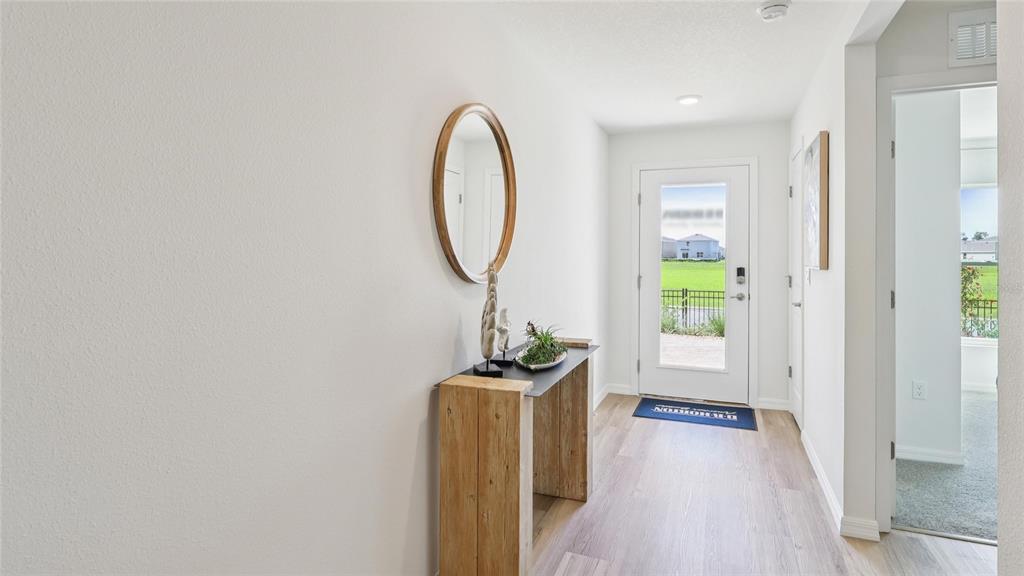 A bright entryway features light wood-look flooring, a rustic console table, and a round mirror — 13042 SW 88TH COURT, OCALA, FL