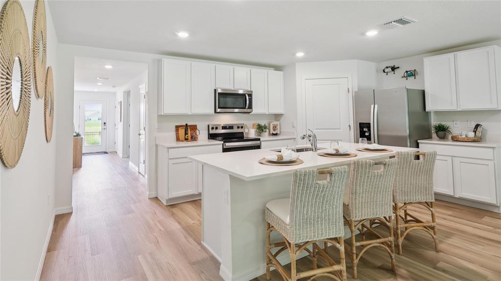 A bright kitchen features white cabinetry, a central island with bar seating, and stainless appliances — 13042 SW 88TH COURT, OCALA, FL