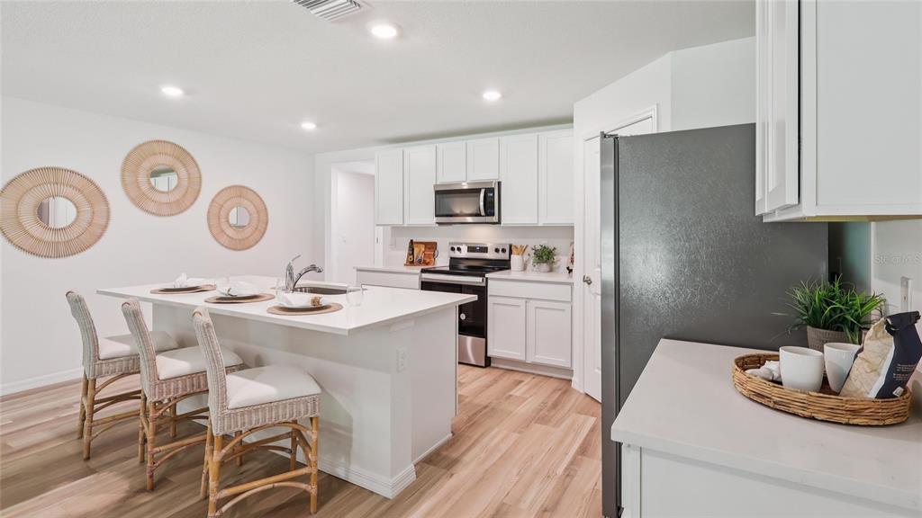 A modern kitchen features white cabinets, a central island with bar stools, and wood flooring — 13042 SW 88TH COURT, OCALA, FL