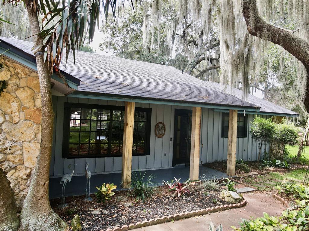 A single-story house with stone siding, a covered porch with wood posts, and Spanish moss trees — 2430 W COUNTY ROAD 44, EUSTIS, FL