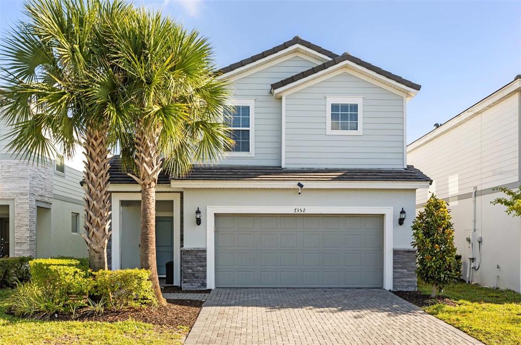 A two-story house with light blue siding, a gray garage door, and a palm tree — 7352 OAKMOSS LOOP, DAVENPORT, FL