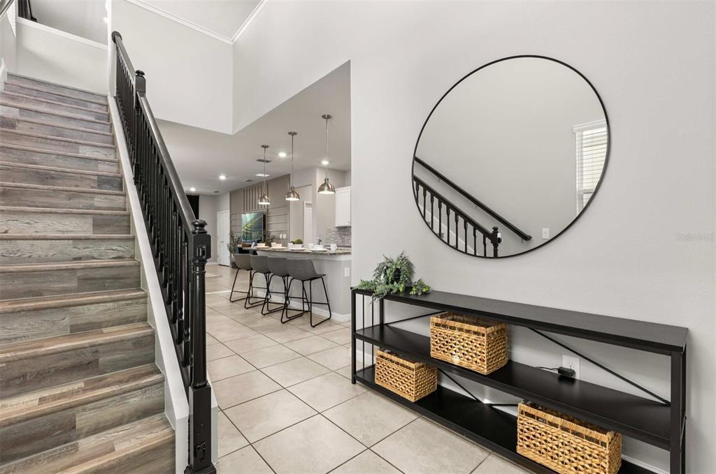 An entryway features a staircase with wood-look treads, a black console table, and a round mirror — 7352 OAKMOSS LOOP, DAVENPORT, FL