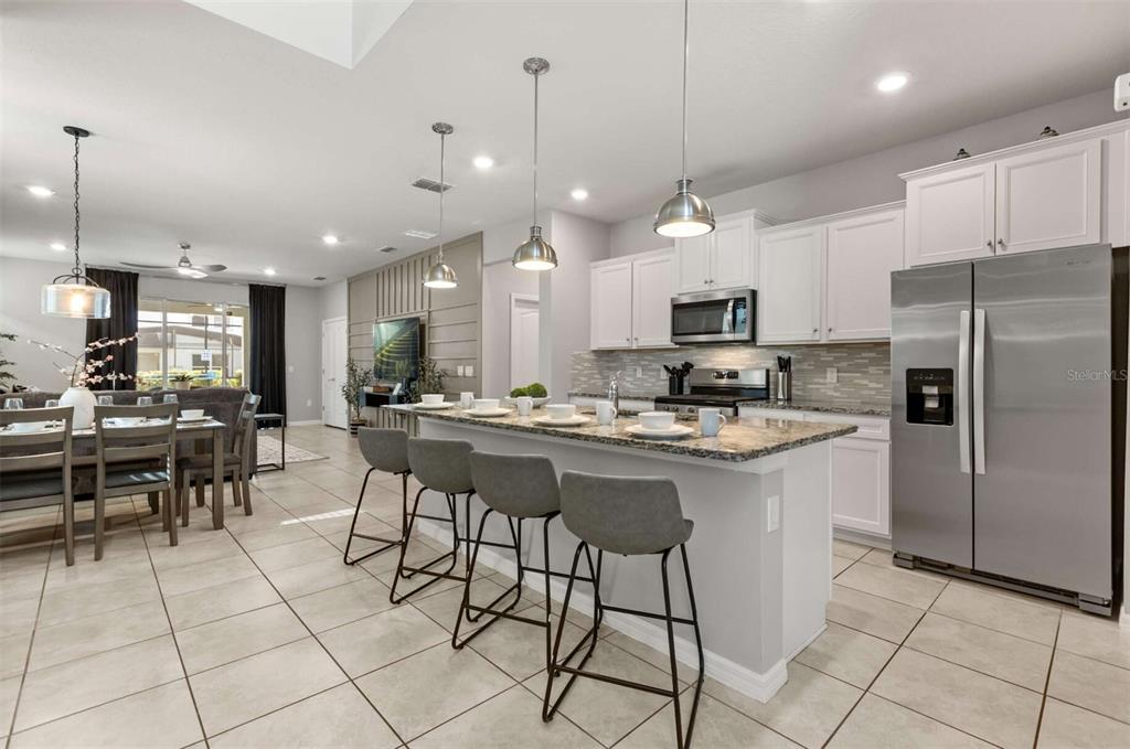 A kitchen with white cabinets, granite countertops, a breakfast bar, and stainless steel appliances — 7352 OAKMOSS LOOP, DAVENPORT, FL