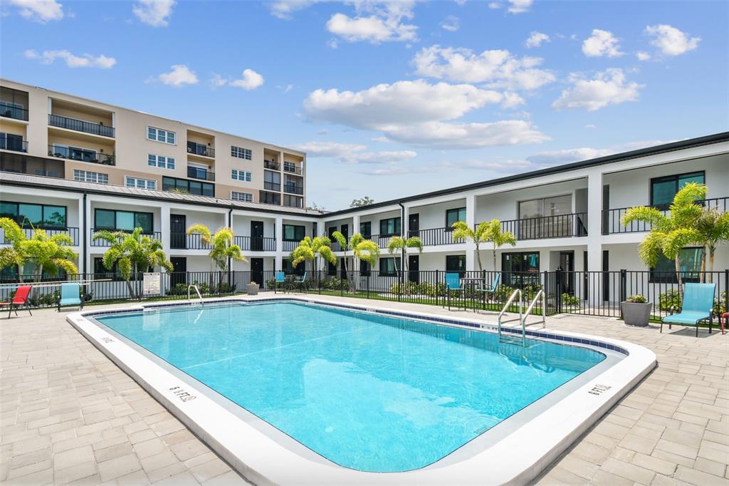 A rectangular swimming pool sits in a courtyard surrounded by two-story apartment buildings and palm trees — 2942 W BAY DRIVE UNIT 8, BELLEAIR BLUFFS, FL