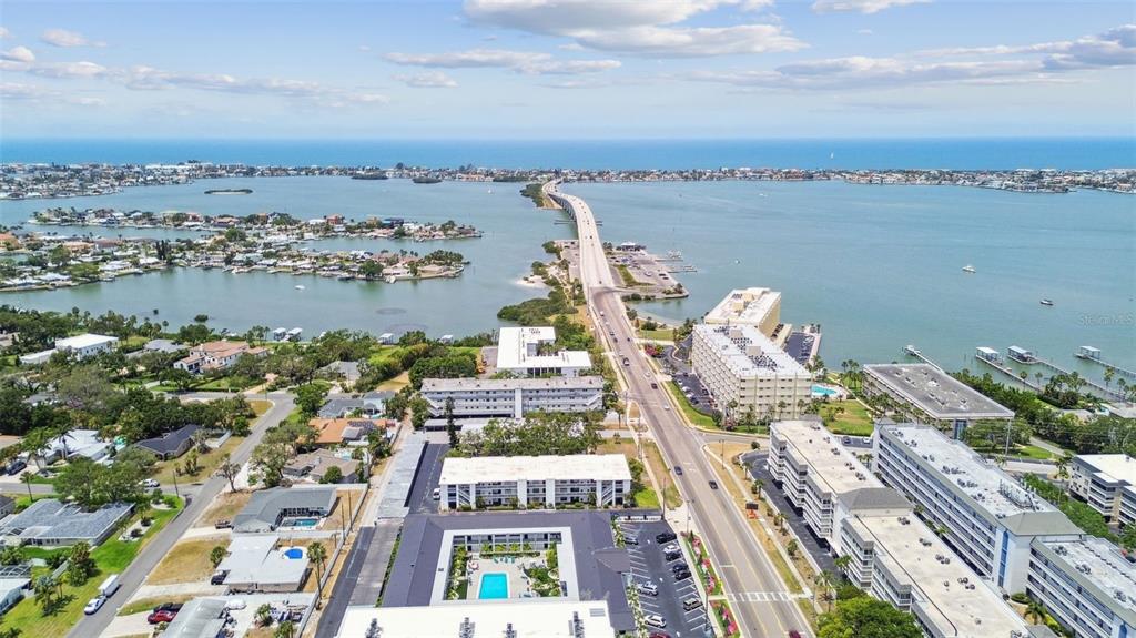 An aerial view shows a coastal neighborhood with apartment complexes, a bridge, and the ocean — 2942 W BAY DRIVE UNIT 8, BELLEAIR BLUFFS, FL