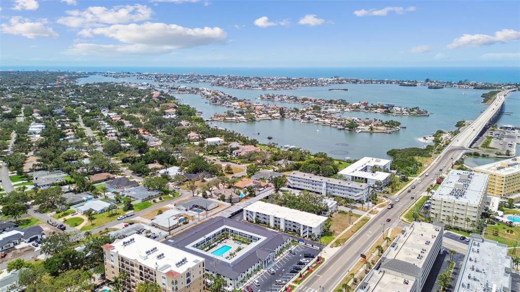 An aerial view shows a coastal neighborhood with multi-story apartment buildings, a swimming pool, and a bridge — 2942 W BAY DRIVE UNIT 8, BELLEAIR BLUFFS, FL