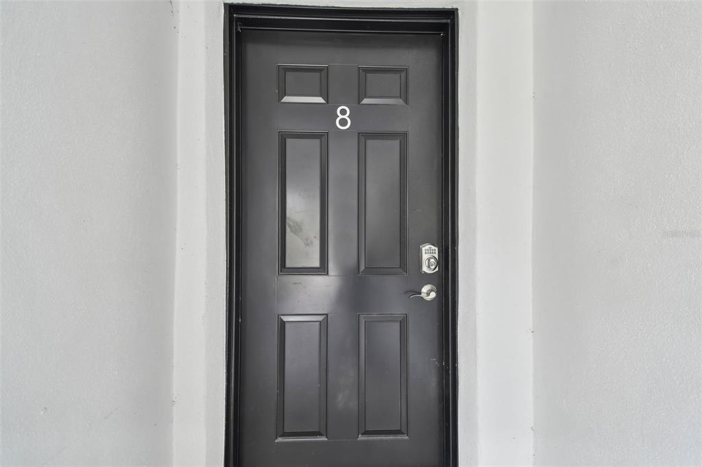 A black front door with the number eight is centered on a plain gray wall — 2942 W BAY DRIVE UNIT 8, BELLEAIR BLUFFS, FL
