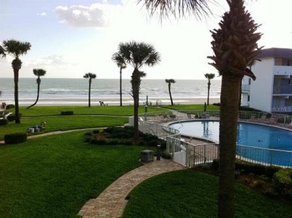 An outdoor view of a swimming pool, a grassy lawn, palm trees, and the ocean — 815 OCEAN SHORE BOULEVARD UNIT 8B, ORMOND BEACH, FL