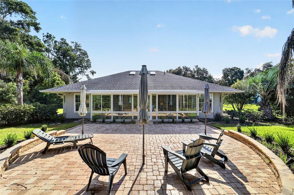 A paved patio with outdoor furniture sits in front of a house with large windows — 9636 SW 190TH TERRACE ROAD, DUNNELLON, FL
