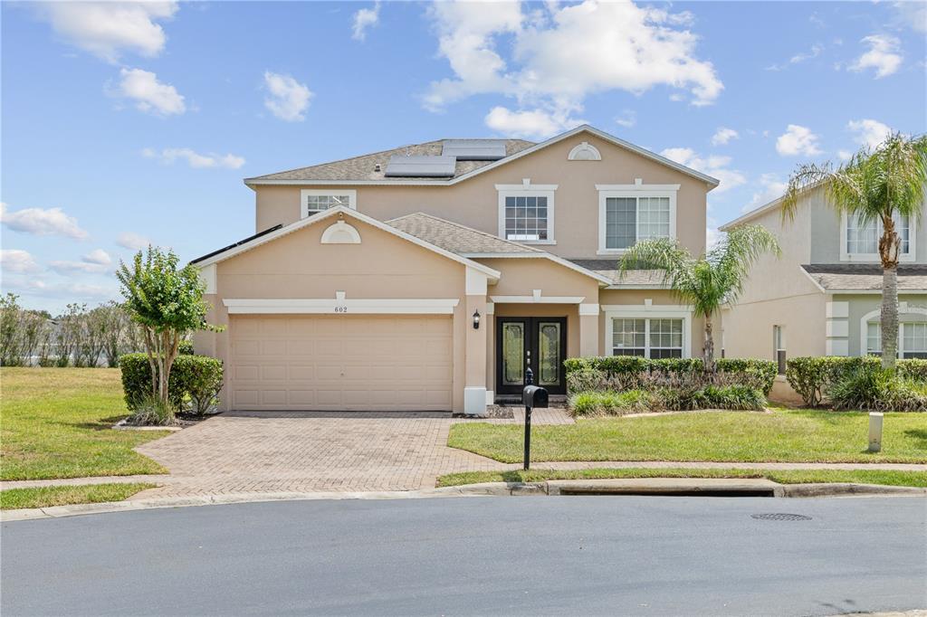 A two-story suburban house with a tan stucco exterior, a two-car garage, and solar panels — 602 HIGHGATE PARK, DAVENPORT, FL