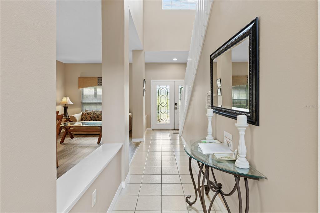 A tiled entryway features a glass console table, a wall mirror, and a staircase — 602 HIGHGATE PARK, DAVENPORT, FL