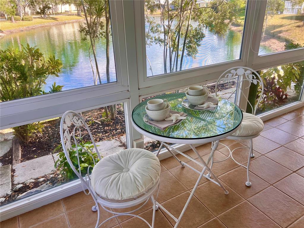 A small bistro table and chairs sit on a tiled sunroom floor overlooking a pond — 7801 ONTARIO STREET CIRCLE, SARASOTA, FL