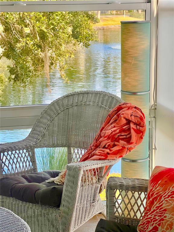 A wicker chair with a coral blanket sits on a sunroom porch overlooking a lake — 7801 ONTARIO STREET CIRCLE, SARASOTA, FL