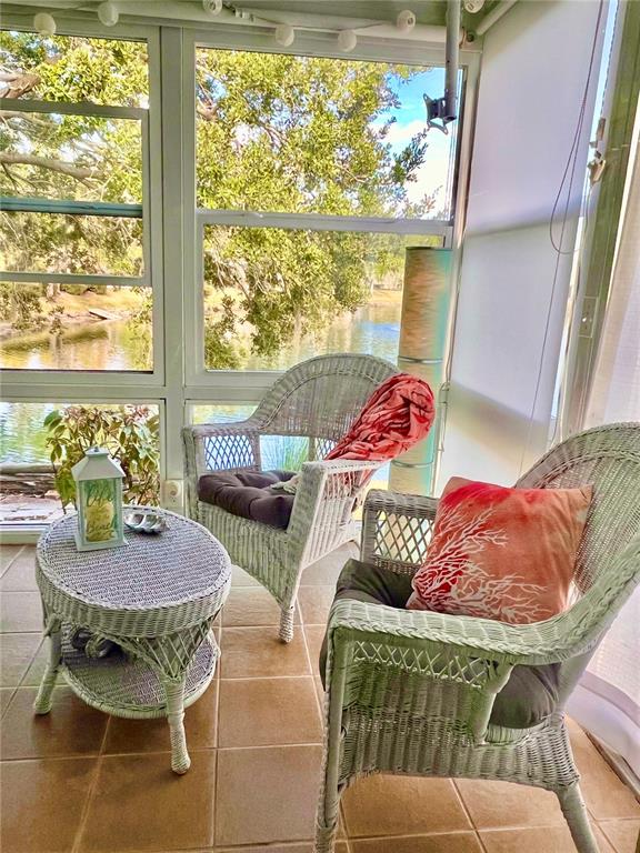 A sunroom features two white wicker chairs and a matching table overlooking a lake — 7801 ONTARIO STREET CIRCLE, SARASOTA, FL